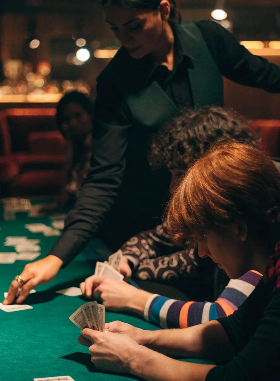 Goście przy stole pokerowym trzymają karty blisko sukna